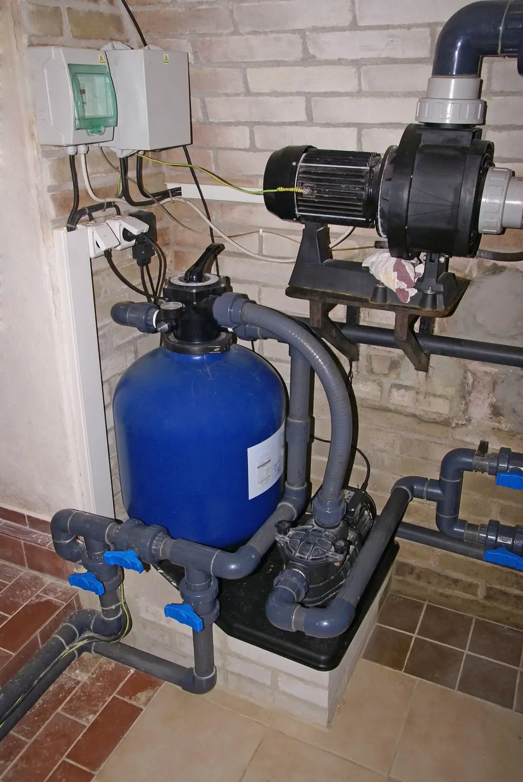 A sand filter tank and pump motor installed on a pool equipment pad